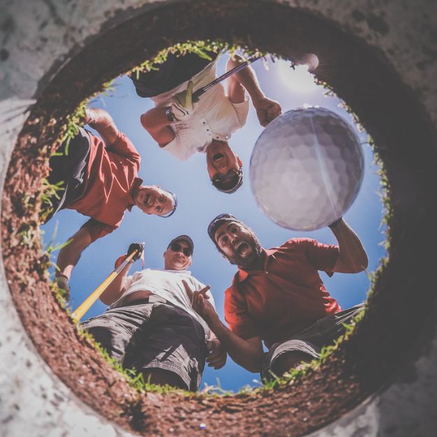 A group of friends looking into the hole and cheering as their golf ball goes in.